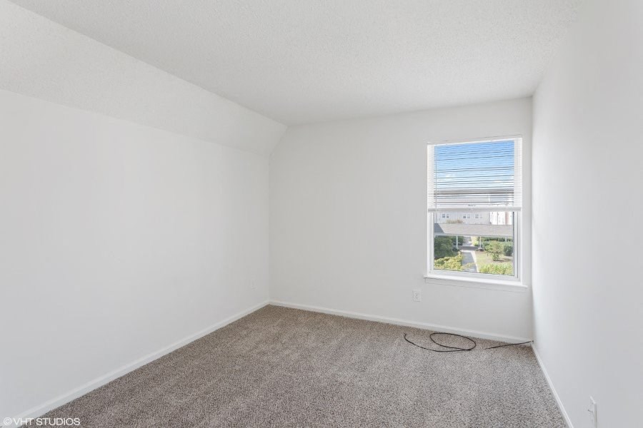 A room with a carpeted floor and a window showing a view of a street.