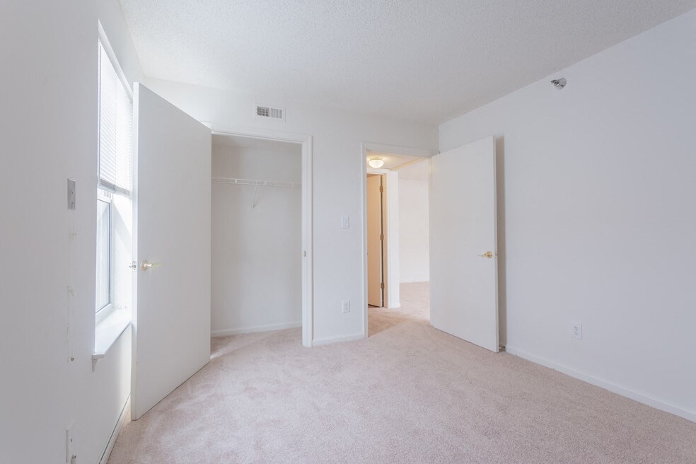 A white room with a carpet floor and a window on the left side.