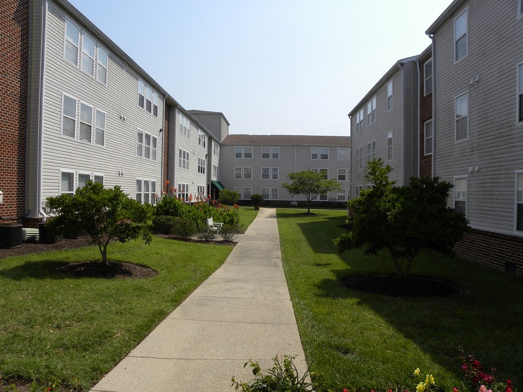 A walkway leads through a grassy area between apartment buildings.