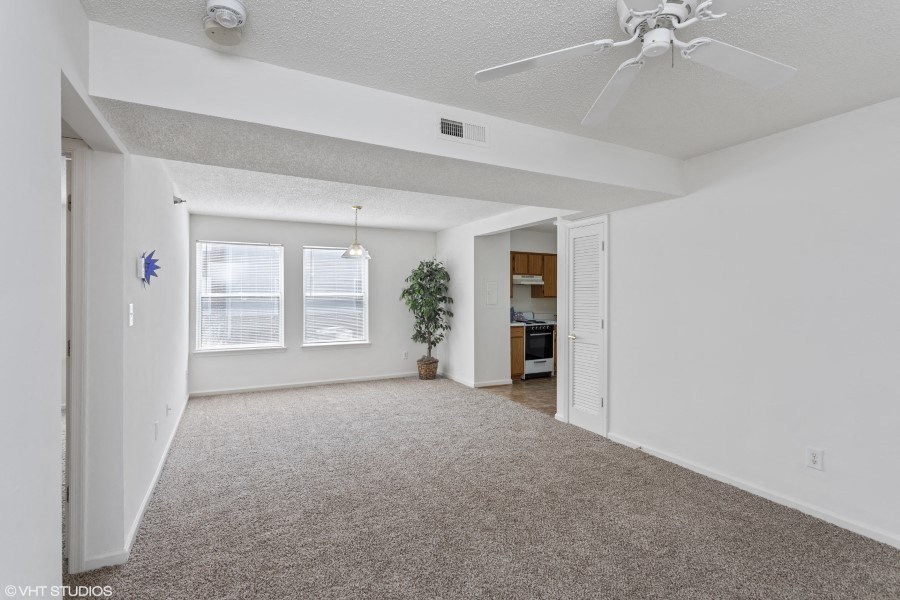 A spacious living room with a ceiling fan and carpeted floor.