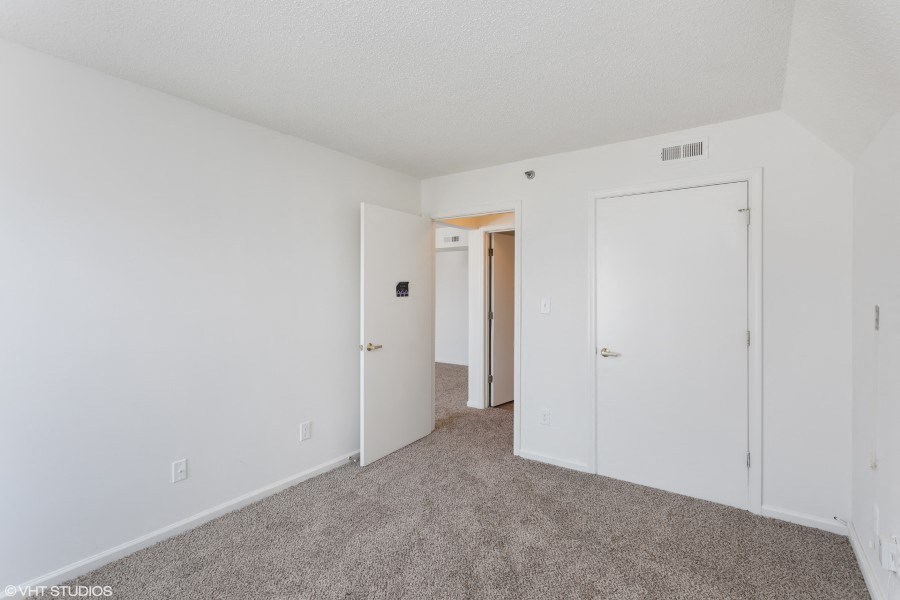 A room with white walls and carpeted floor with three doors.