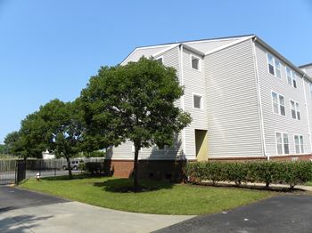 A large white building with a grey roof and a tree in front of it.
