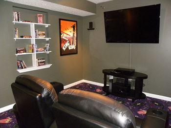 A black leather couch sits in front of a television in a room with a purple carpet.
