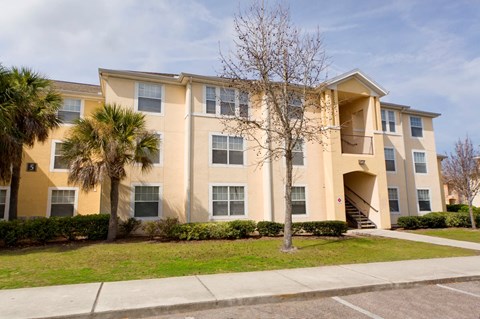 A beige apartment building with a tree in front.
