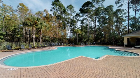 A swimming pool surrounded by trees and a brick patio.