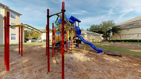 A playground with a red and yellow structure and a blue slide.