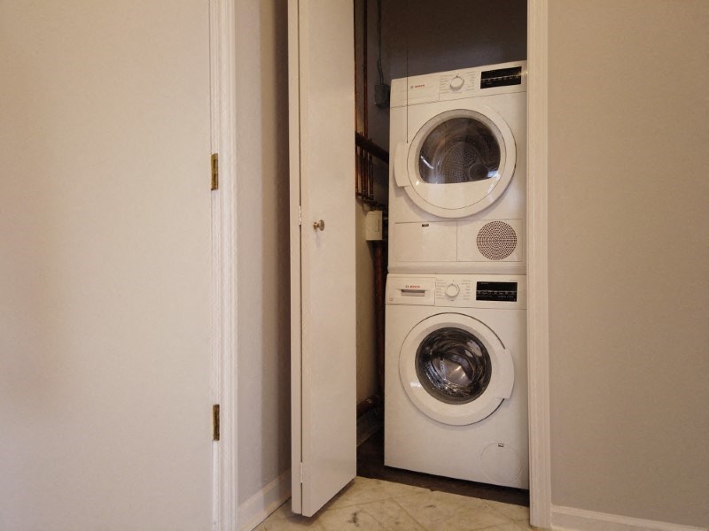 A white washing machine is in a small space between a door and a wall.
