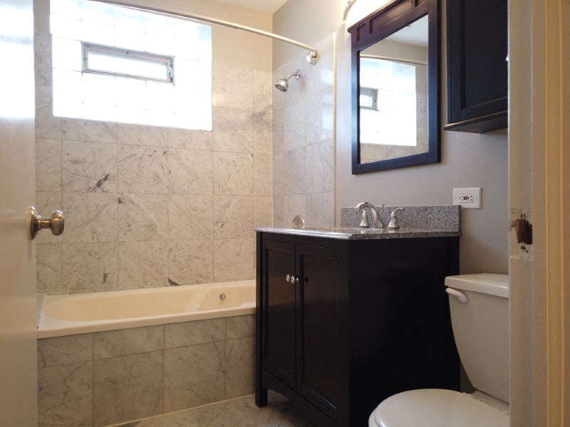 A bathroom with a tub, toilet, sink and mirror.