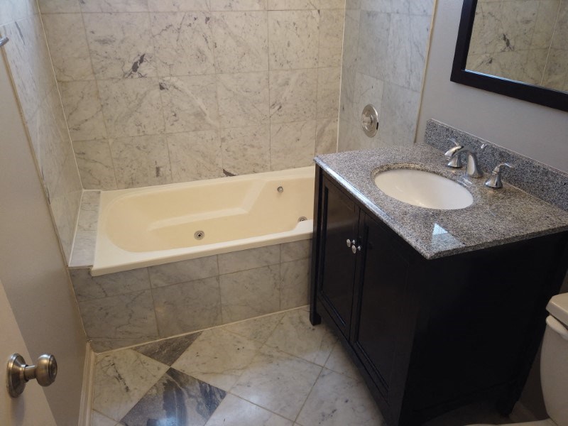 A bathroom with a marble countertop and a white bathtub.