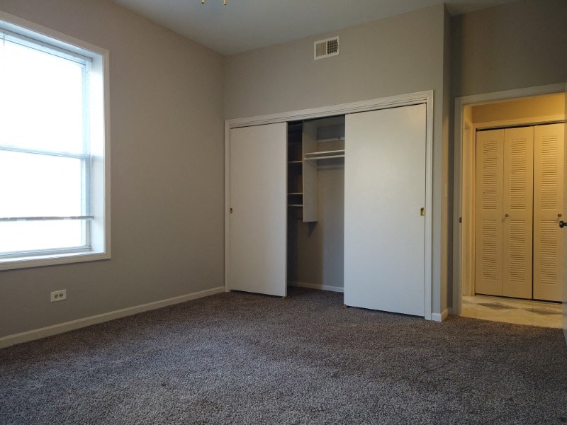 A room with a carpeted floor and a white closet with wooden doors.