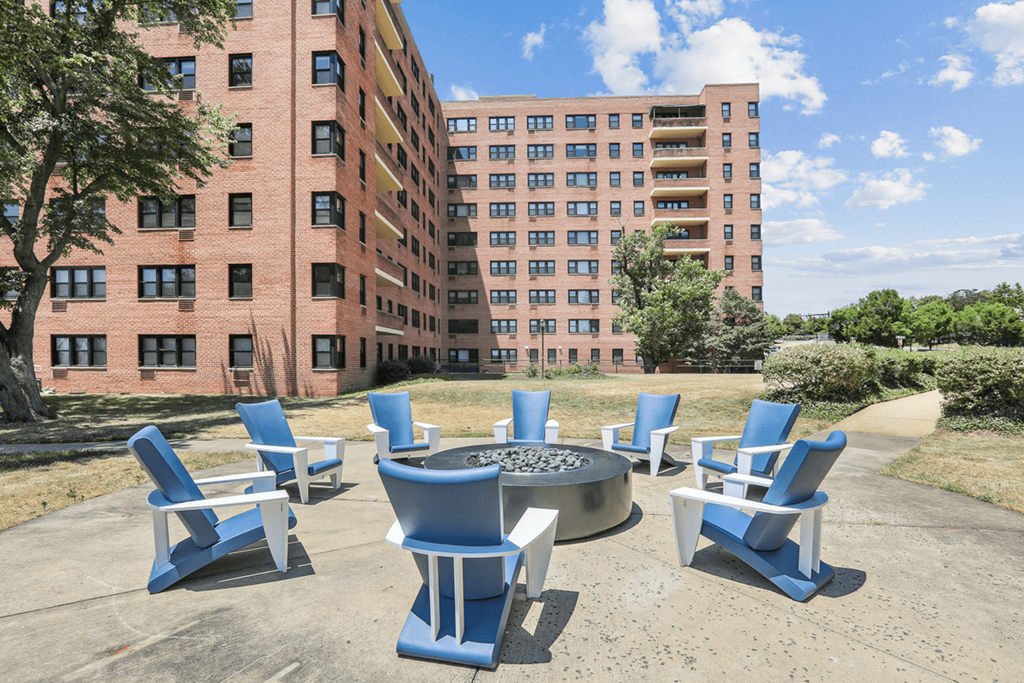 an outdoor patio with blue chairs and a fire pit in front of an apartment building