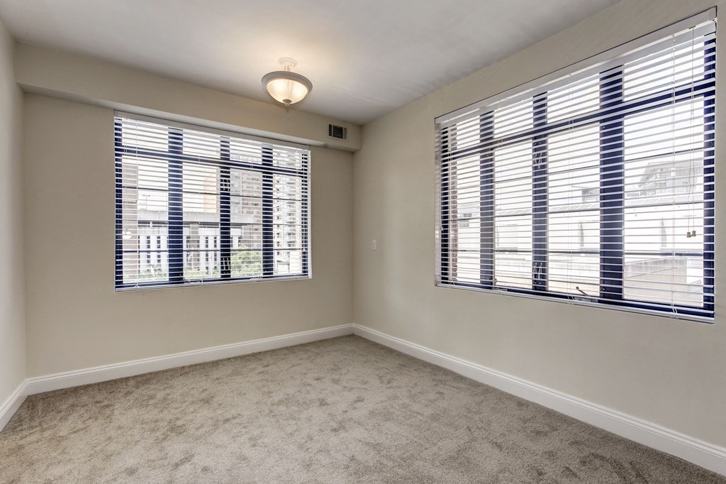 A room with a carpeted floor and two windows covered with blinds.