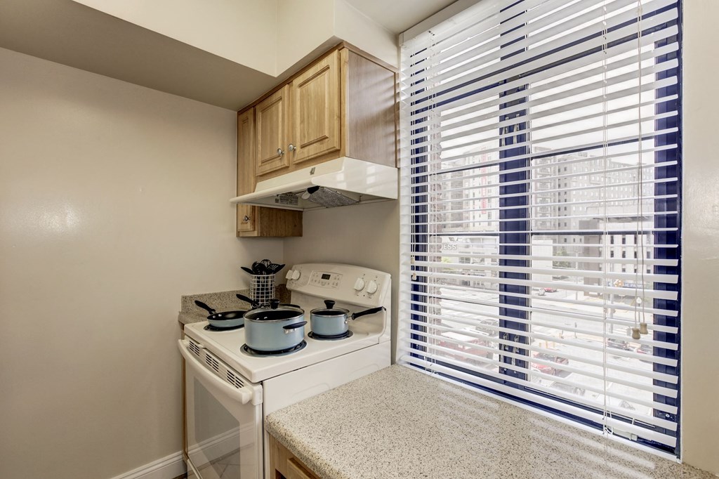 A kitchen with a stove top oven and a window with blinds.