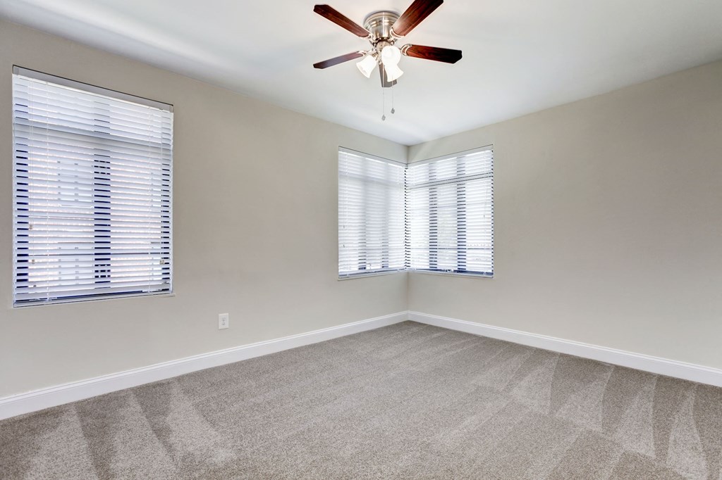 A room with a ceiling fan and two windows with blinds.