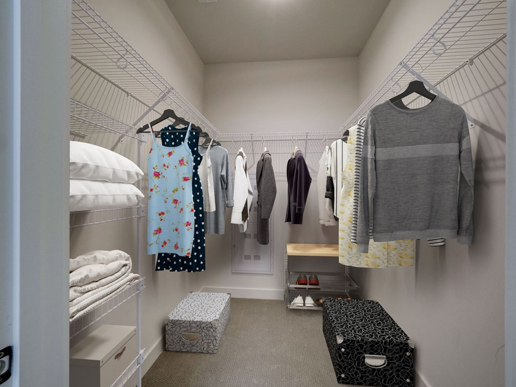 A white closet with clothes hanging and a bench.
