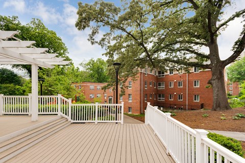 A white fence surrounds a wooden deck with a white pergola over it.