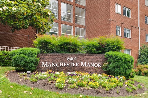 A sign for Manchester Manor in front of a brick building.