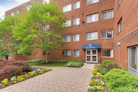 A brick building with a blue awning and a garden in front.