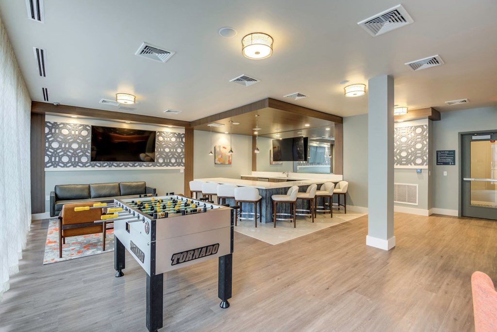 A foosball table is in the middle of a room with a couch and a dining table.