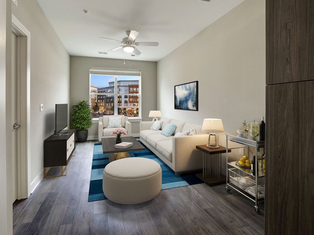A modern living room with a white sofa, a grey ottoman, and a ceiling fan.