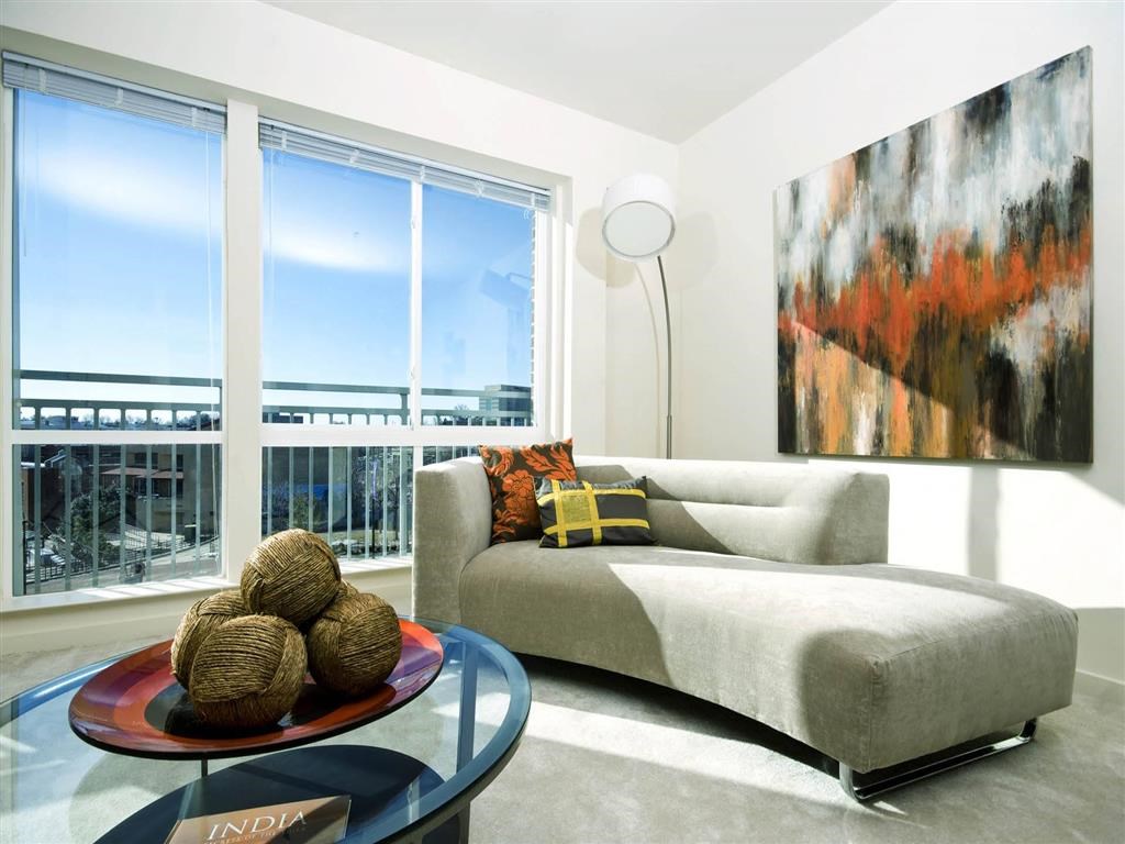 A living room with a grey couch, a glass table, and a large painting on the wall.