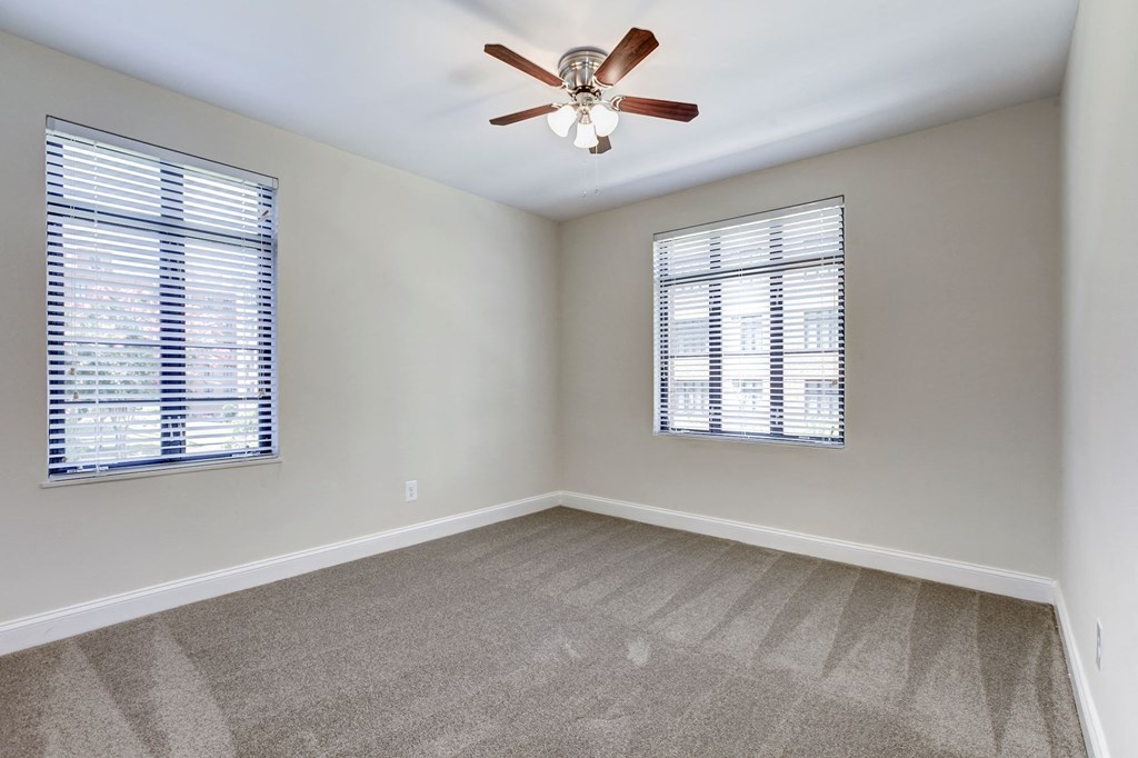 A room with a ceiling fan and two windows with blinds.