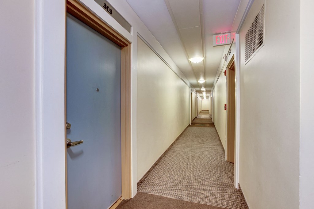 A long hallway with a blue door on the left and a red exit sign on the ceiling.