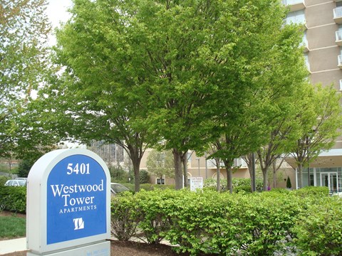 A sign for Westwood Tower Apartments stands in front of a building and trees.