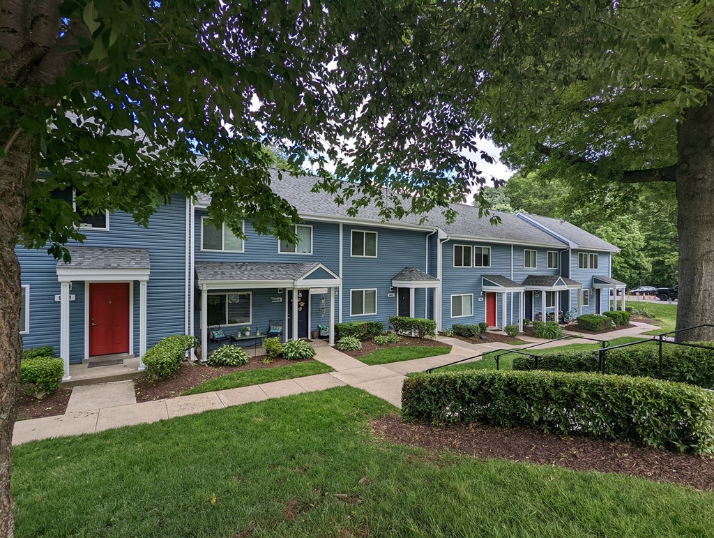 A blue house with a red door is surrounded by greenery.
