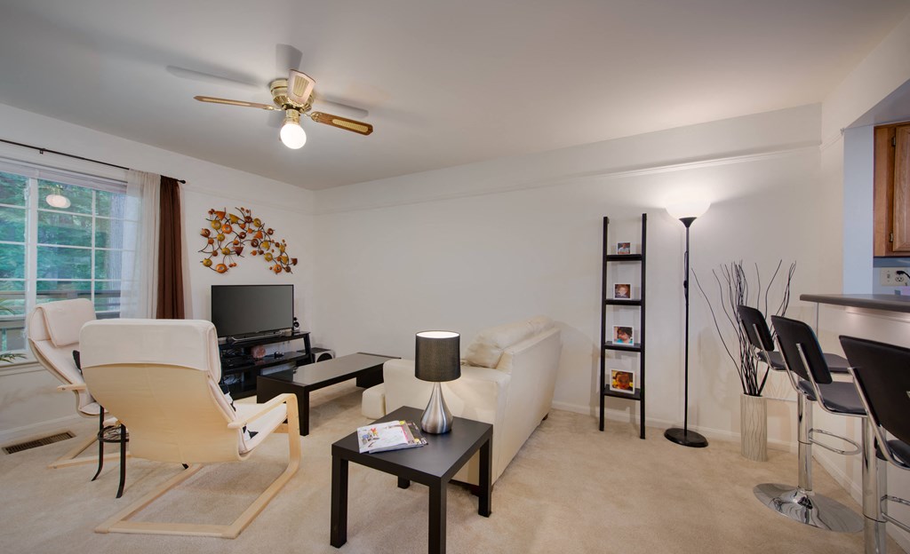 A living room with a television, a chair, a table, and a fan.