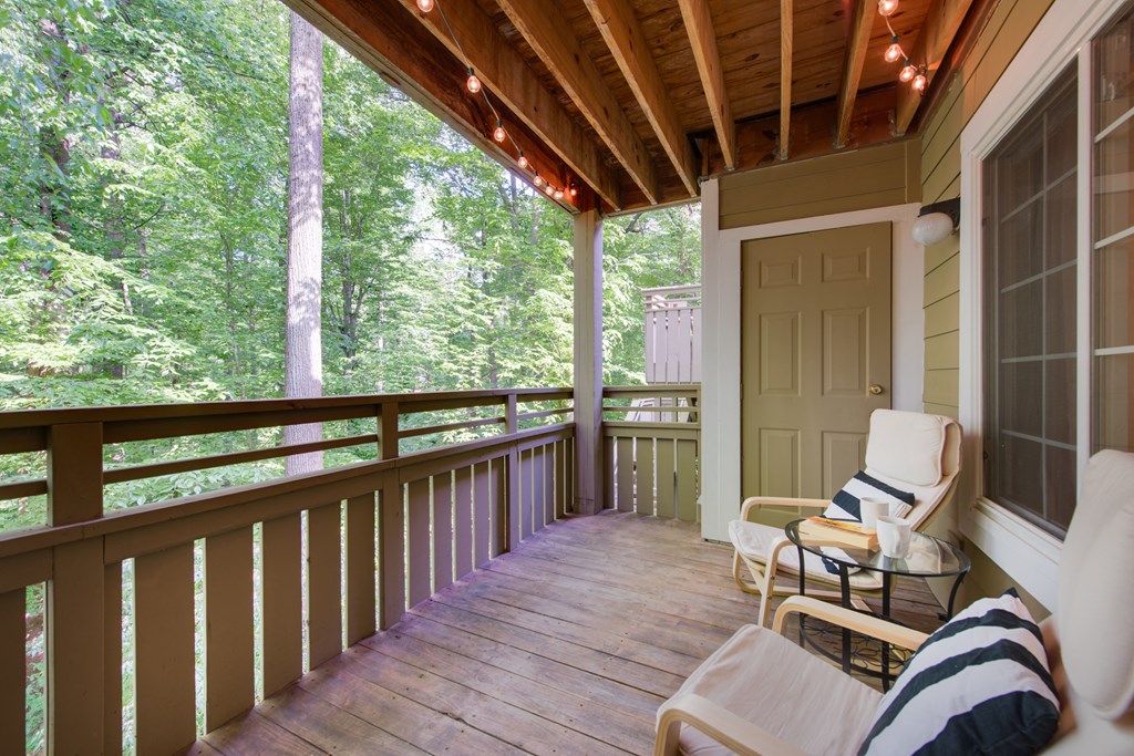 A wooden porch with a white chair and a table with a striped pillow.