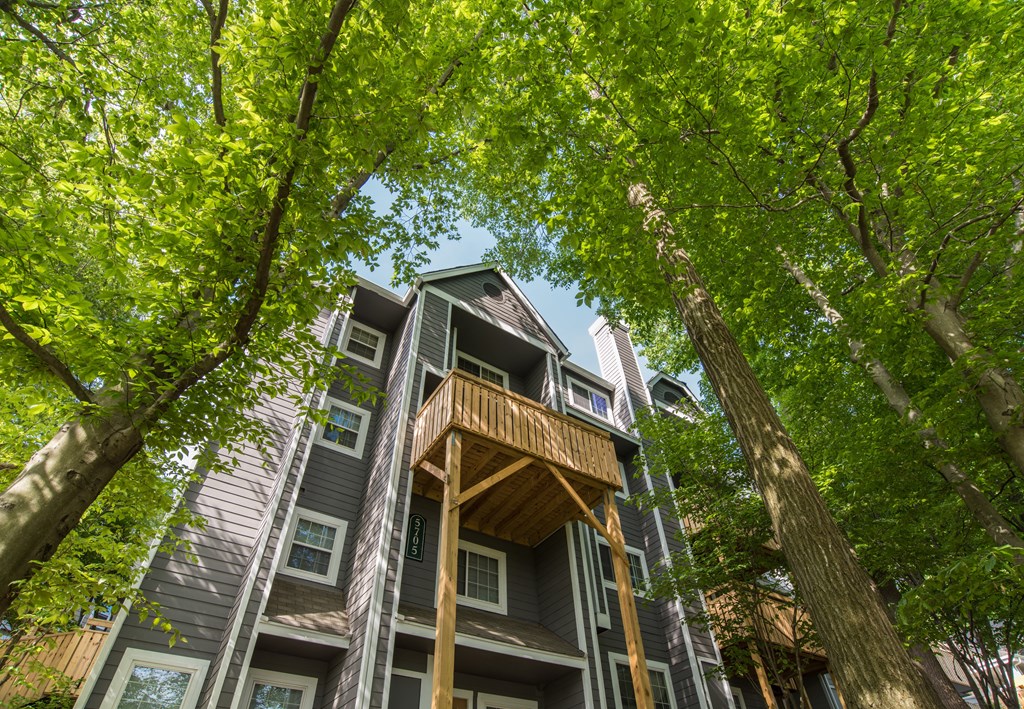 A tall apartment building with a balcony is surrounded by trees.