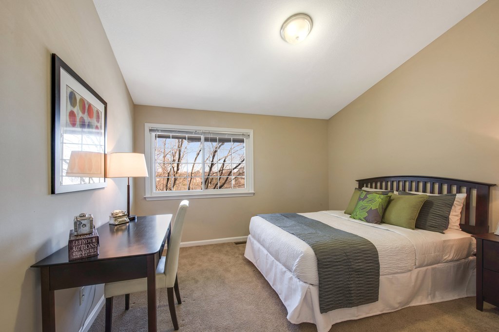 A bedroom with a bed, nightstand, and a table with a lamp.