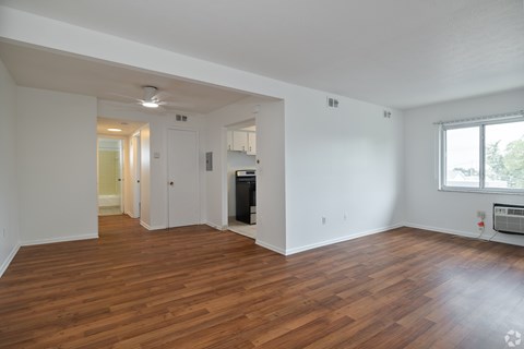 A large empty room with wood flooring and a window.