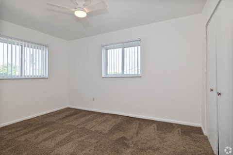 A room with a carpeted floor and two windows.