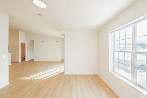 A large empty room with wooden floors and a window overlooking a snowy landscape.