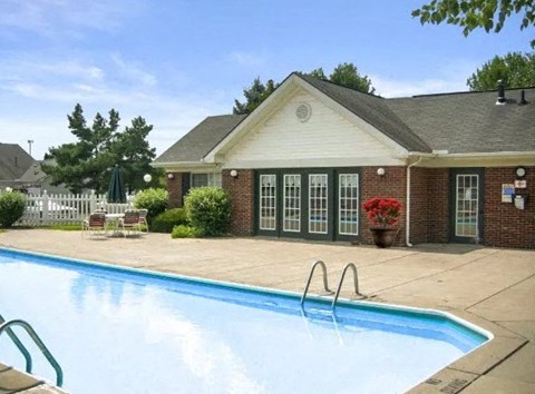 A pool in front of a house with a white picket fence.