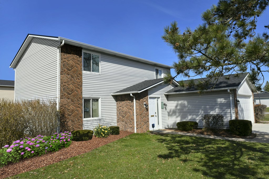 a white house with a stone wall and a white garage