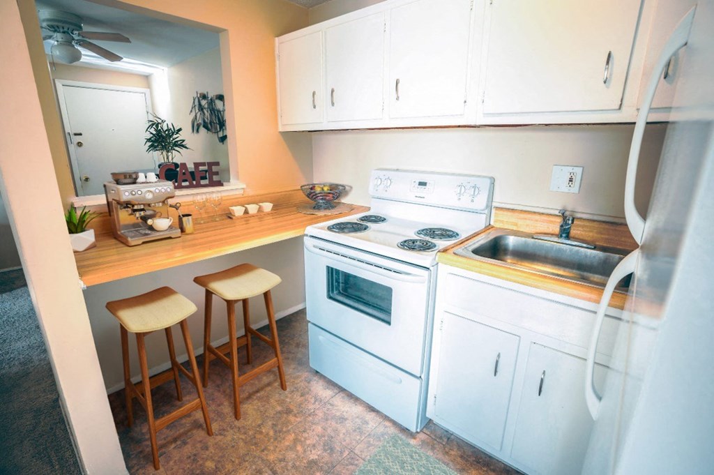 a kitchen with white appliances and a counter with two stools