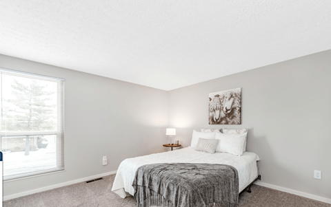 A bedroom with a bed, nightstand, and a painting on the wall.