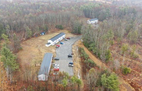 Fall aerial view of Clark's Mills showing two-story apartment buildings along a paved driveway and parking, surrounded by woods