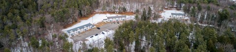 Winter aerial view of Clark's Mills apartments on Little Falls Road in Hollis, Maine, with two-story buildings set among pine woods