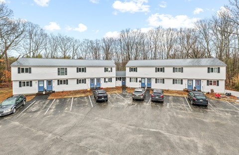 Front exterior of Hilltop's two-story townhouse-style apartment buildings with blue entry doors and a paved parking lot