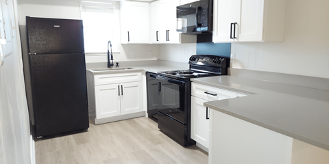 A black refrigerator is in a kitchen with white cabinets.