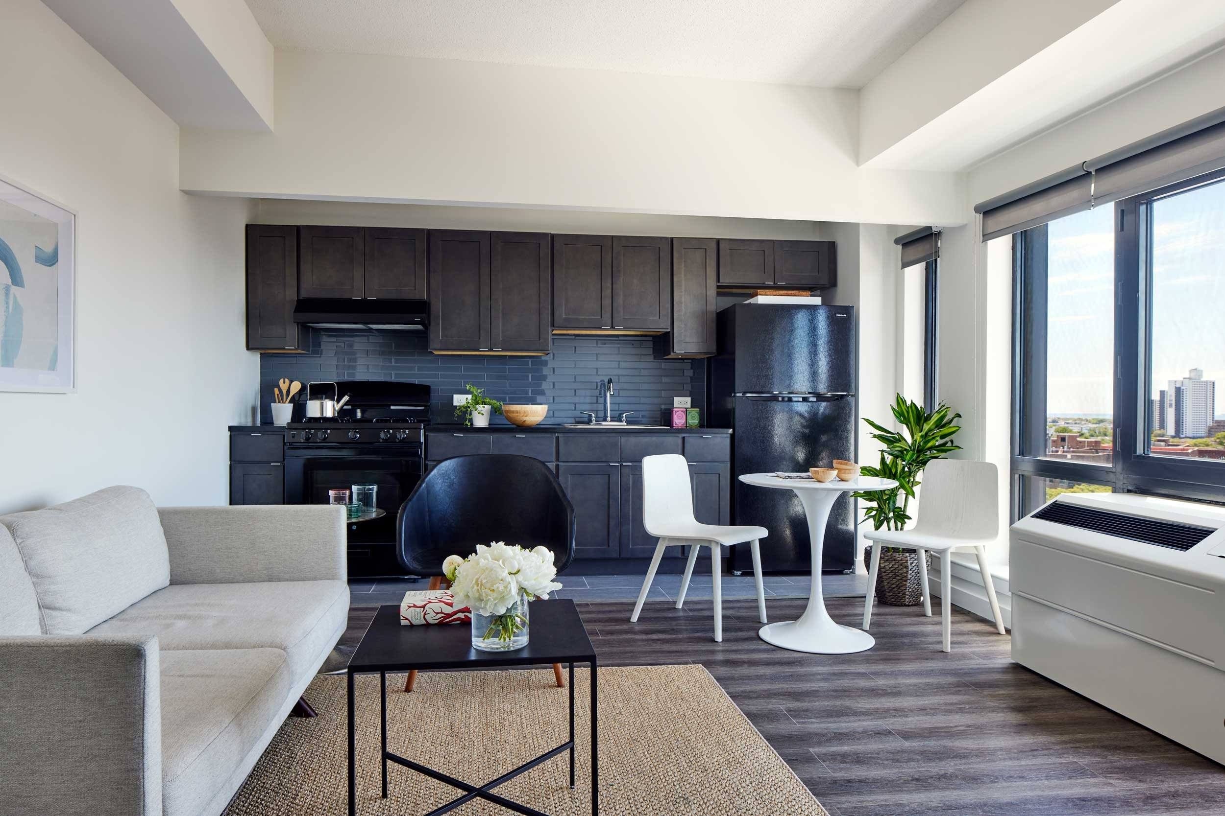 A modern living room with a grey sofa, a black coffee table, and a black kitchen area.