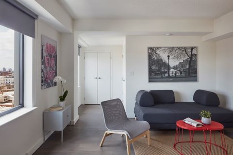 A living room with a grey couch, a red table, and a painting on the wall.