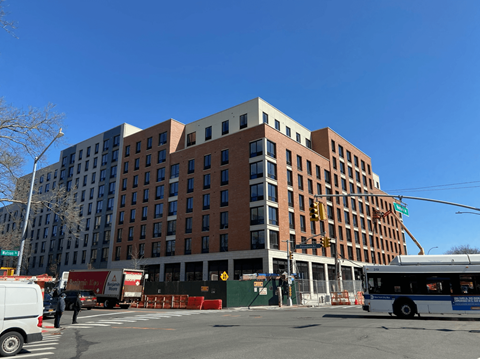 A large multi-story building with a red brick facade and a white van and bus in front of it.