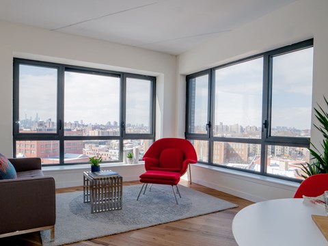 A red chair sits in a white room with a view of the city.