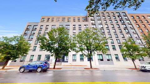 A blue car is parked on the street in front of a multi-story building.