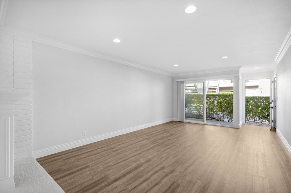a living room with white walls and a wooden floor and a glass door